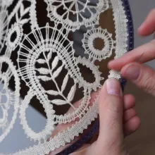 Klöppelstück wird in Rahmen aus dem 3D-Drucker genäht