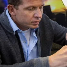 Goldschmied bei der Arbeit in seiner Werkstatt: Mit einem kleinen Hammer bearbeitet er konzentriert ein Schmuckstück im Schraubstock unter einer Lupenleuchte.