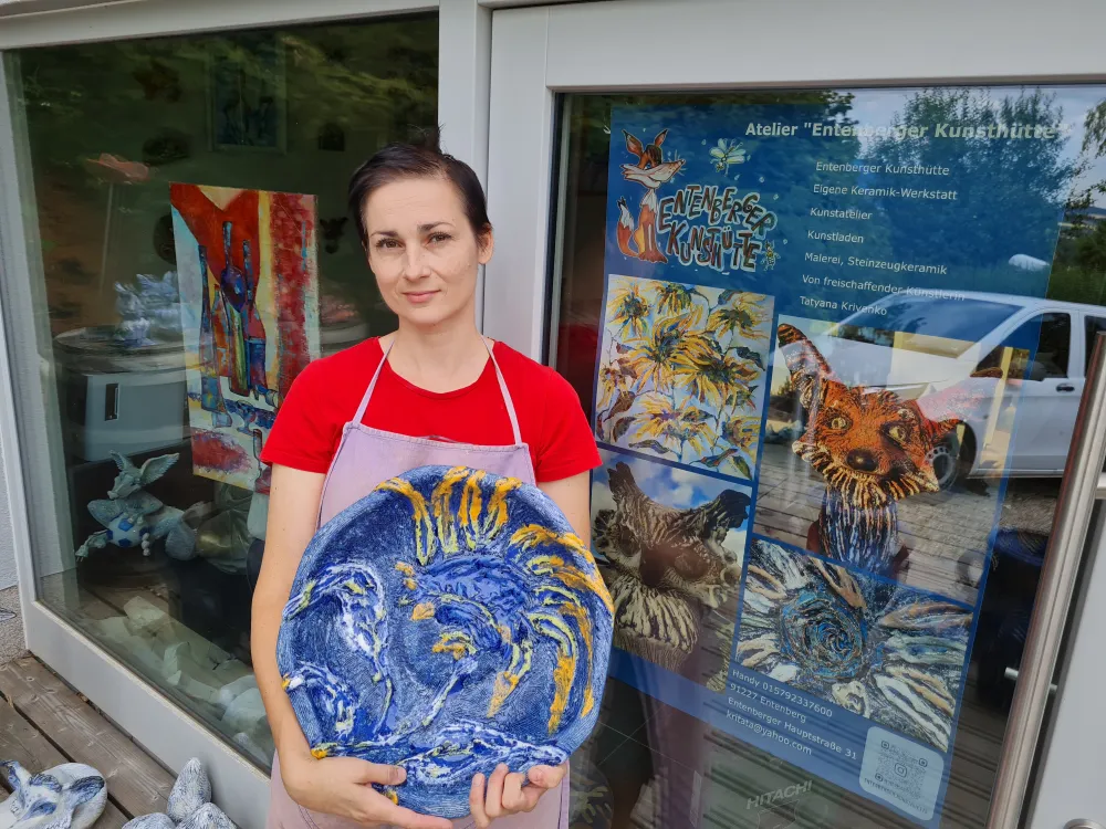 Ich stehe vor dem Eingang zum Atelier mit einer blau-gelben Keramikschale