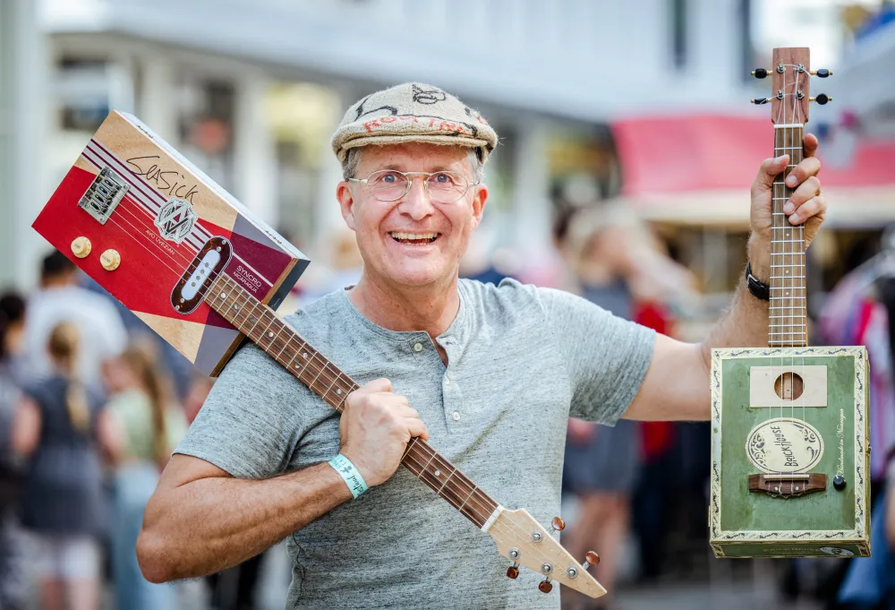 Turinsky mit Mütze aus einem alten Kartoffelsack. Hält zwei Instrumente in die Luft.