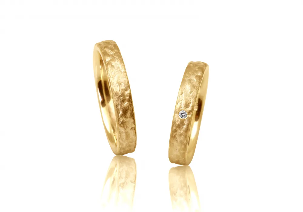 Zwei Partnerringe aus Roségold, je 4mm breit, die eine strukturierte Oberfläche besitzen, die an Baumrinde erinnert. Im kleineren der beiden Ringe ist ein Brillant mit 0,02 Carat in sehr guter Qualität eingefasst.