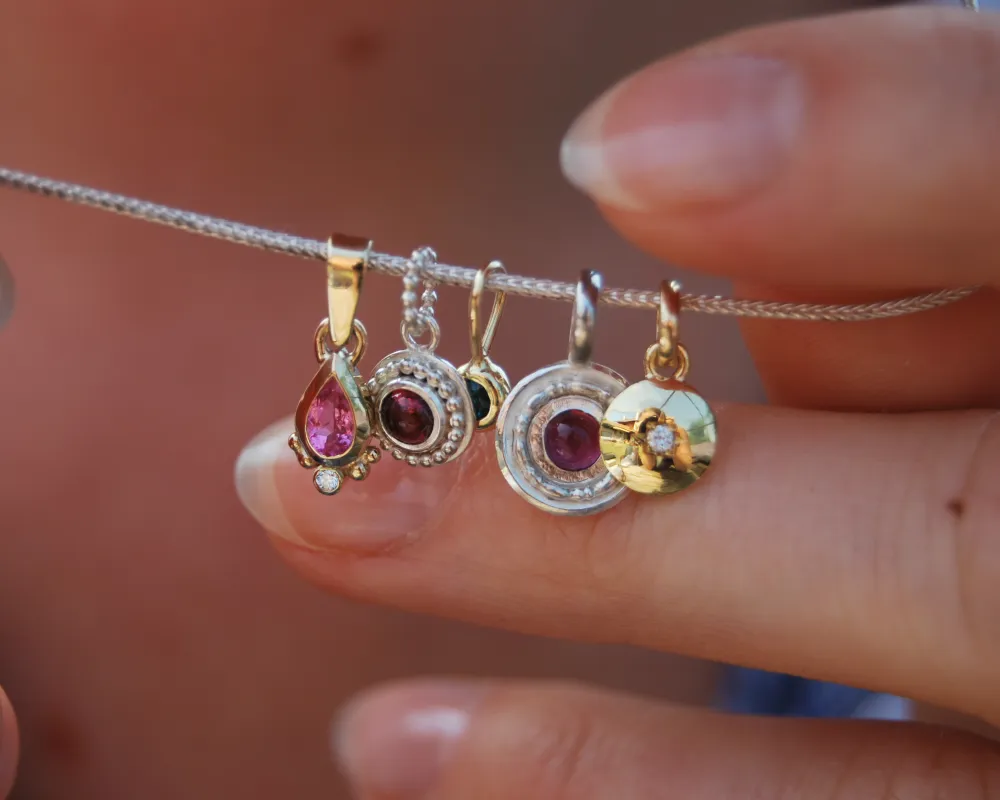 Diverse Anhänger aus Gold und Silber mit bunten Edelsteinen.