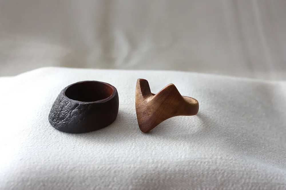 zwei handgefräste Ringe: einer ist breit und aus Avocadokernholz, der zweite ist aus Olivenholz mit einem abstrakten Fuchskopf.