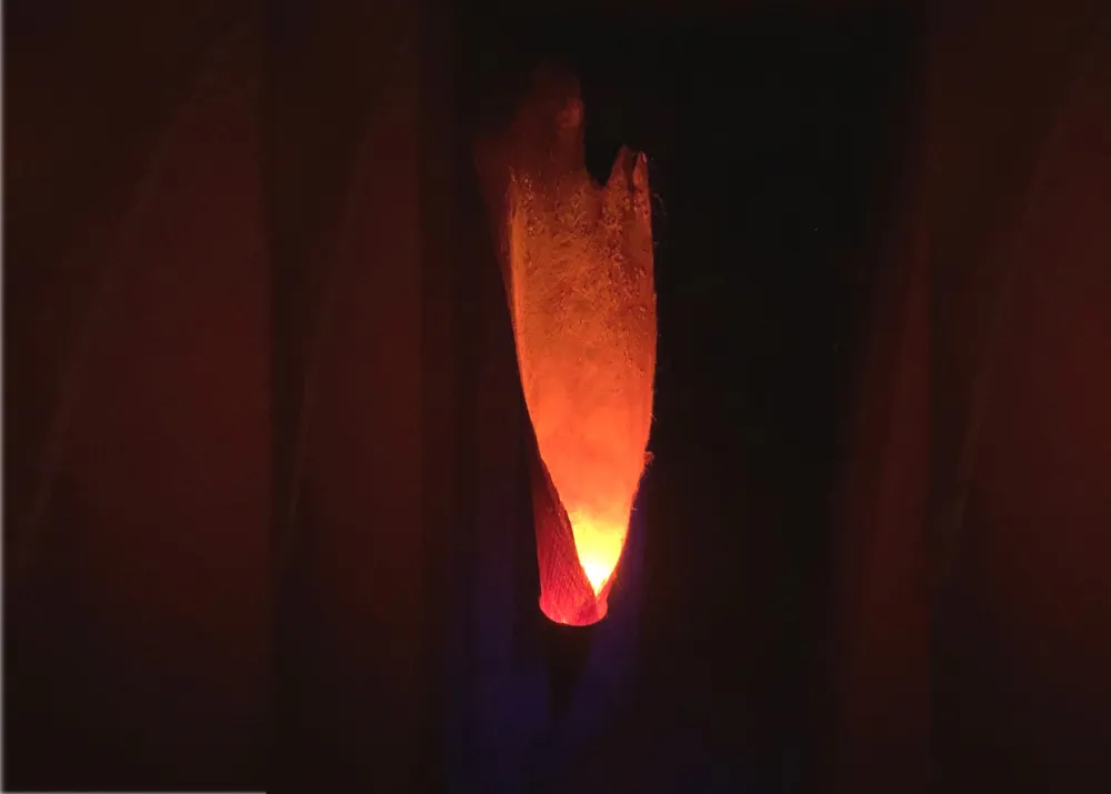 Flame- Naturmaterialien (Stein; Kupfer; gefärbte Palmfaser) sind geschickt miteinander verbunden und erzeugen durch eine Feuereffekt-Led-Lampe eine menschgroße Flamme.