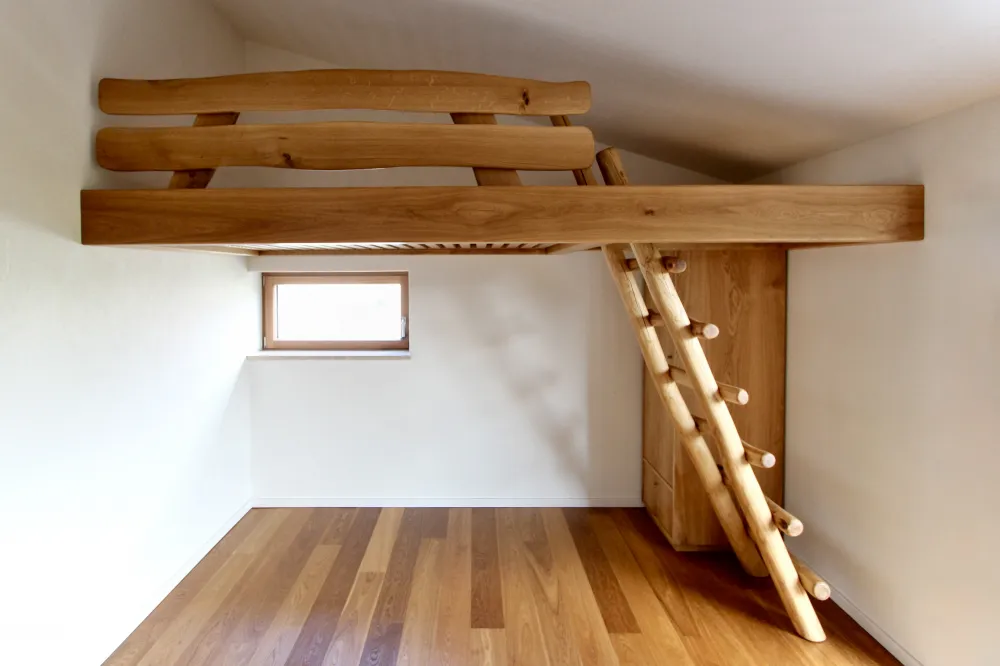 Hochbett aus Eiche-Massivholz, welches freitragend von Wand zu Wand reicht. Aufstieg aus Robinien-Rundholz. Entworfen und gefertigt von Sinnesmagnet, der Möbeltischlerei in Dresden