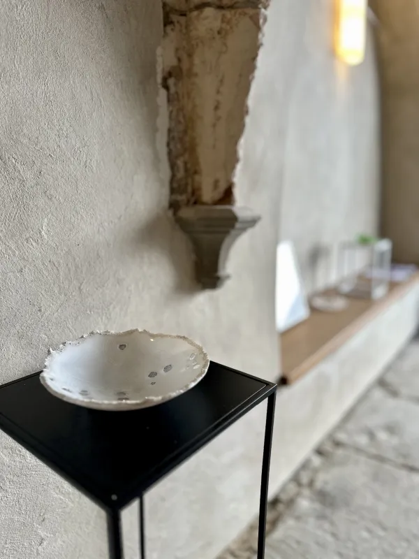 Eine Schale aus weißem Glas auf einem schwarzen Sockel aus Metall. Der Sockel steht in einer Ausstellung.