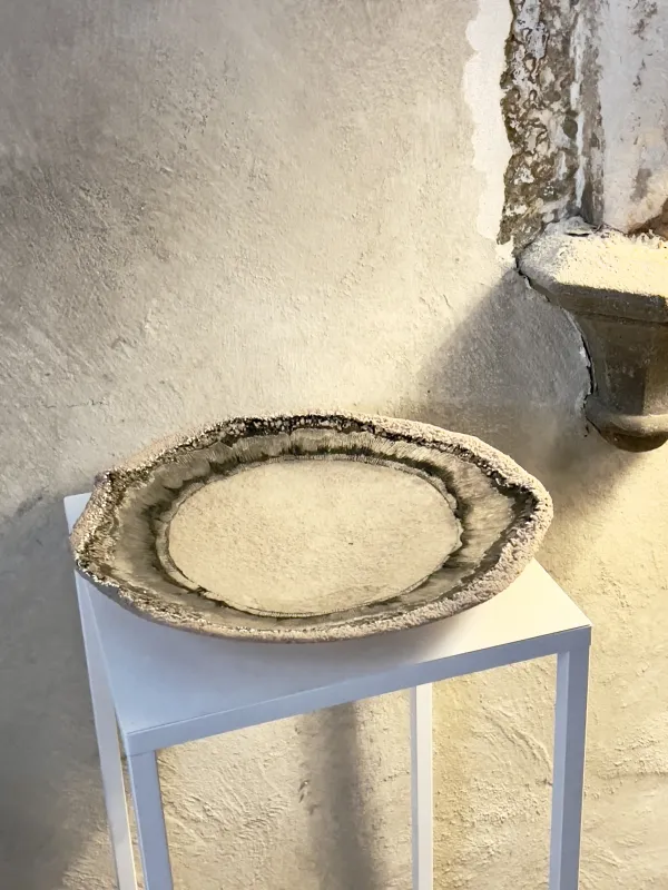 Eine Schale aus Glas auf einem weißen Sockel aus Metall. Die Schale ist mit schwarzer Farbe bemalt. Der Sockel steht in einer Ausstellung.