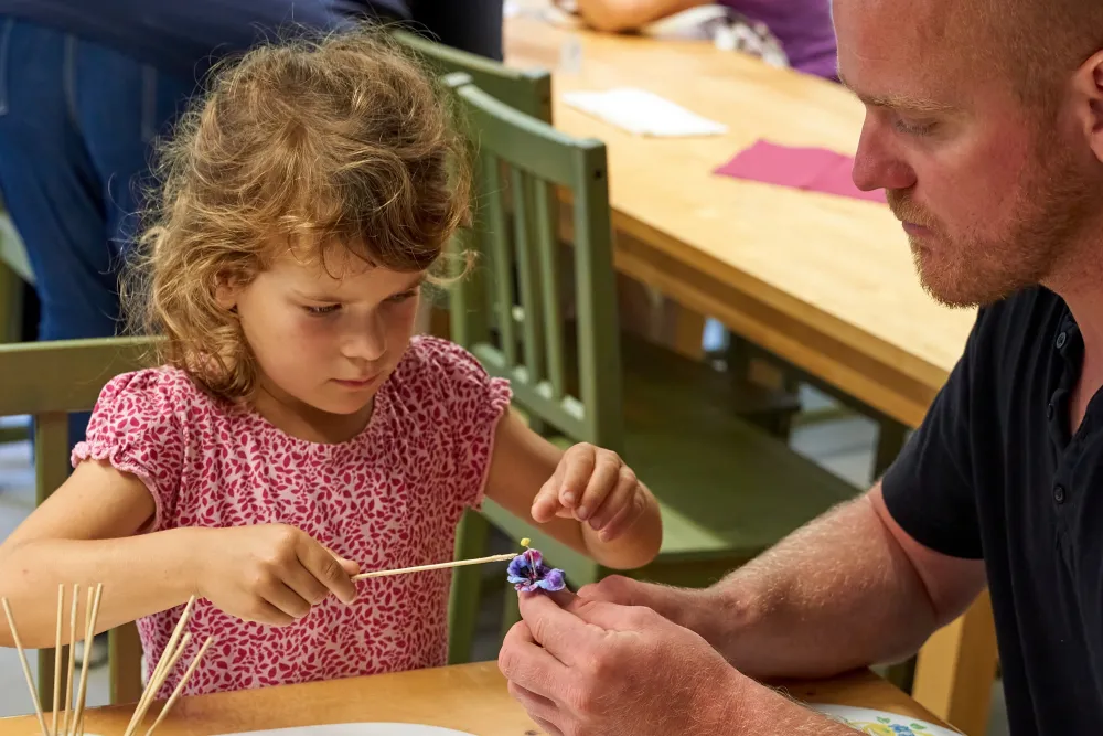 ein Mädchen bemalt eine Blüte während ihr Vater die Blume festhält