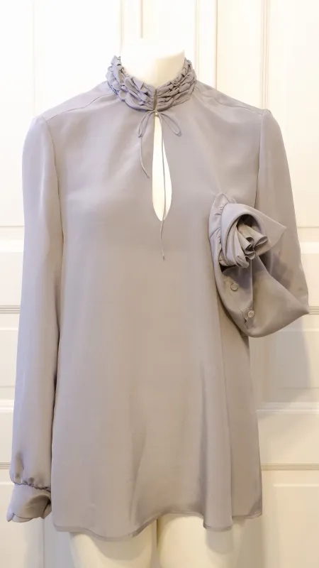 Klassische Seidenbluse mit interessantem Stehklagen. Der Kragen wird mit einer zarten Seidenkordel aus dem selben Stoff mit einer Schleife geschlossen. 