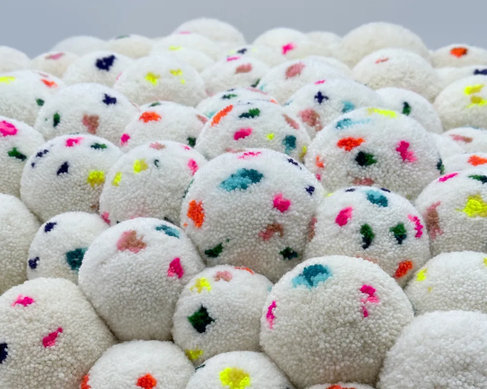 Detailaufnahme Weißes Pompon-Kissen mit bunten Farbtupfern 