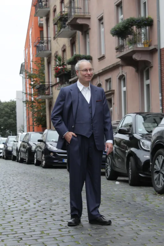 Ein eleganter Herr auf einer Straße, der einen dreiteiligen blauen Anzug trägt.