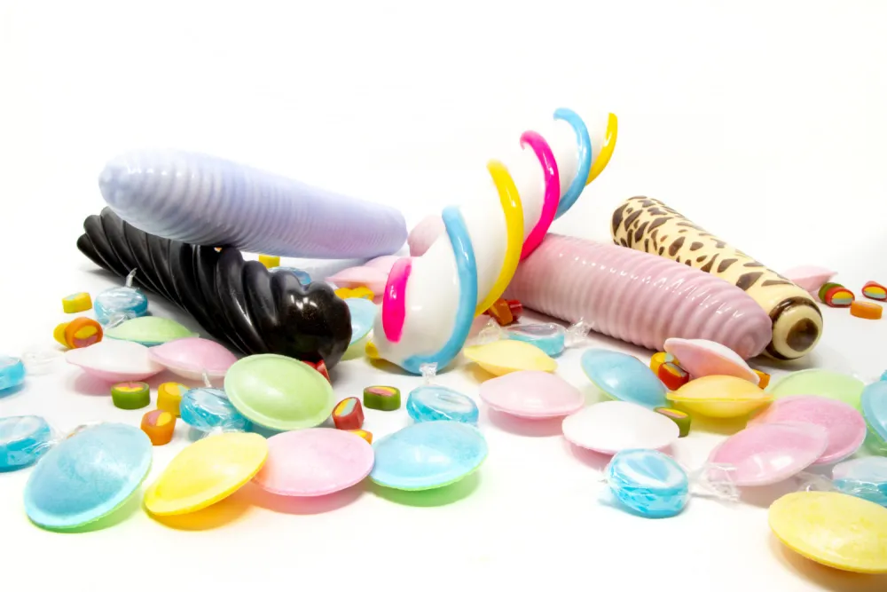 bunte Dildos in Form von Mäusespeck, Lakritzstange und Zuckerwatte liegen zwischen Süßigkeiten