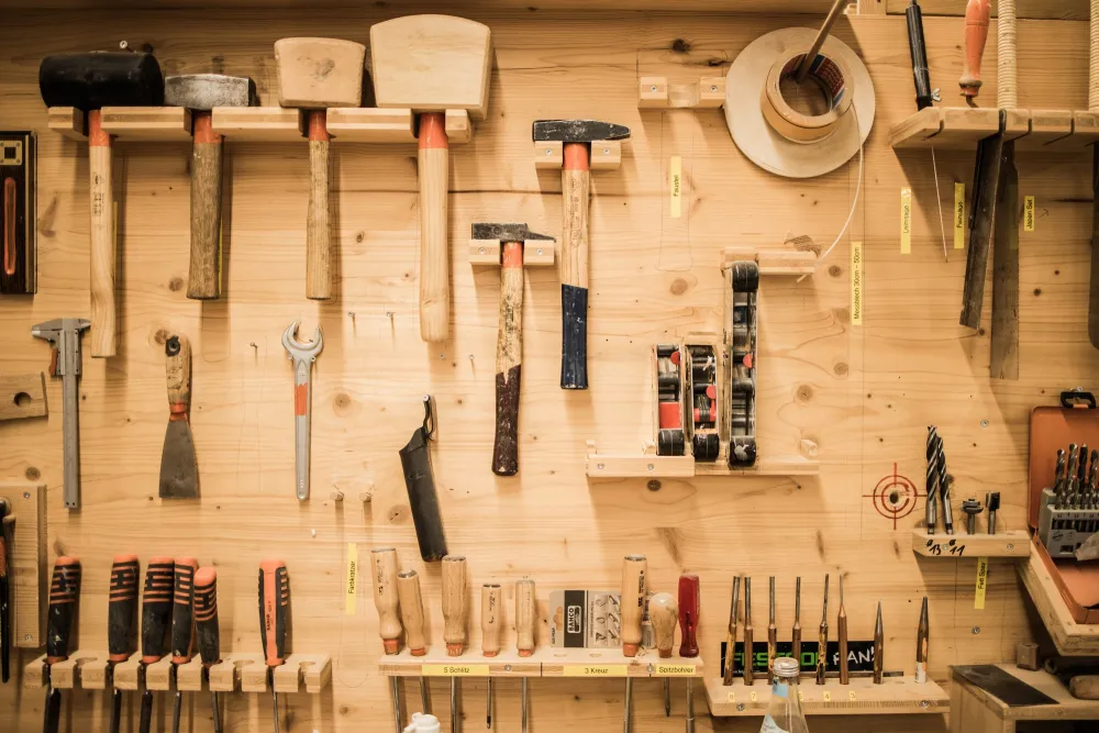 Eine Detailaufnahme einer Werkbank. Man sieht Stechbeitel, Hammer, Sägen und weitere Werkzeuge, die von Personen im Schreinergewerk benötigt werden.